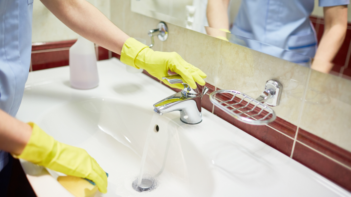chambermaid cleaning sink in bathroom of hotel room